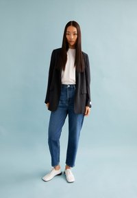 Donkerblauwe pinstripe blazer, witte t-shirt, blauwe jeans en witte veterschoenen. Gladde textuur met een getailleerde pasvorm en recht model.