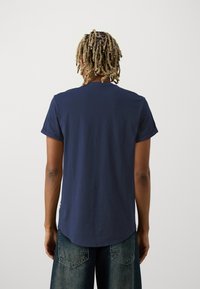 Granatowy bawełniany t-shirt z okrągłym dekoltem, krótkimi rękawami i zakrzywionym dołem, zestawiony z wyblakłymi niebieskimi dżinsami.