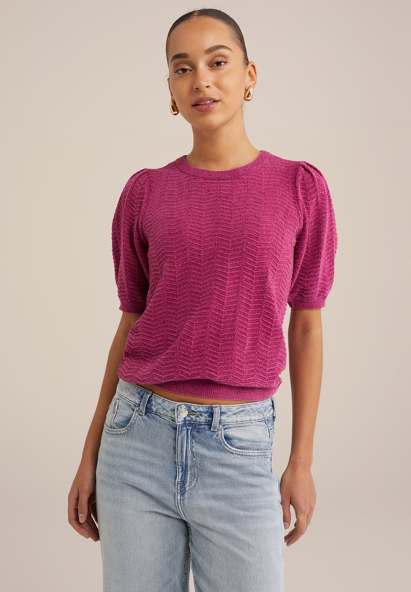 Maglione a maniche corte di colore fucsia in maglia, con un motivo a zigzag testurizzato, scollo rotondo e orlo a coste, abbinato a jeans azzurri a vita alta.