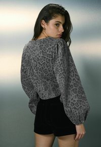 Bluză cu imprimeu leopard gri, cu mâneci voluminoase și un design scurt, asortată cu șorturi negre. Textură fină, cu manșete elastice.