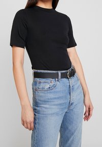 Top fitted a maniche corte nero abbinato a jeans di denim azzurro chiaro a vita alta, con una cintura nera e una fibbia circolare argento.