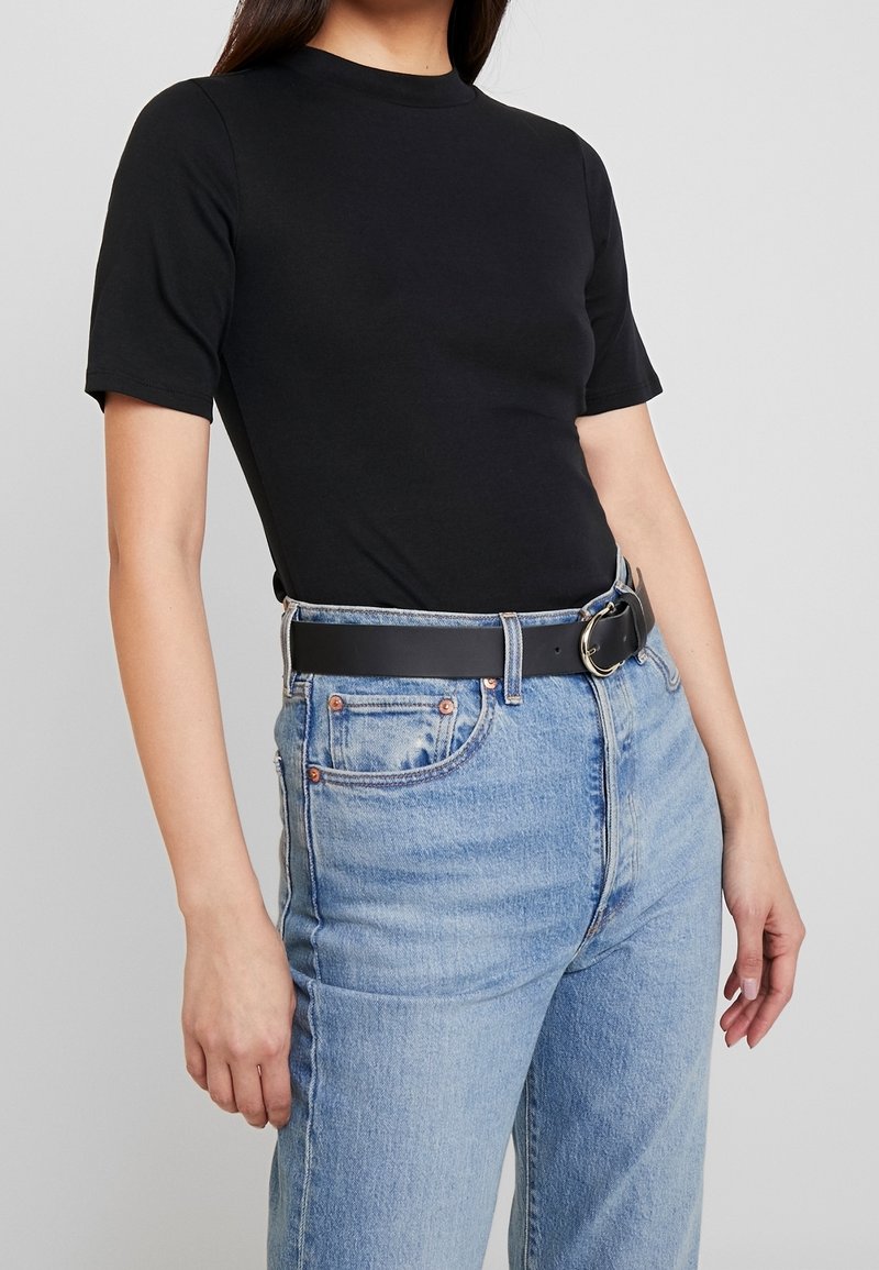 Top fitted a maniche corte nero abbinato a jeans di denim azzurro chiaro a vita alta, con una cintura nera e una fibbia circolare argento.
