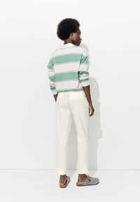 Pull-over rayé vert, rose et blanc avec un col, associé à un pantalon blanc et des chaussures à enfiler à imprimé léopard, vu de dos.