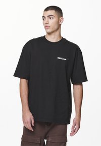 Black cotton t-shirt with a relaxed fit and short sleeves. Features a small white logo on the left chest area. Smooth texture.