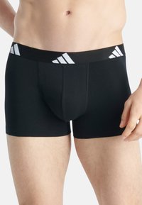 Svarta boxertrosor i ett stretchigt material, med en bred midjeresår som har vita Adidas-loggor och en åtsittande design.