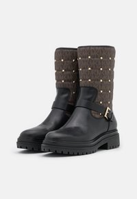 Svarta läderankelboots med ett kviltat brunt tygskaft, prydda med guld nitar och en sidrem med spänne. Chunky, texturerad sula.