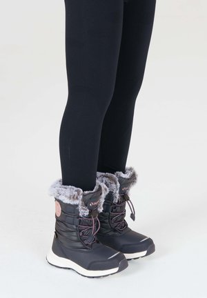 Schwarze wasserdichte Winterstiefel mit Kunstfellaufschlag, Schnürdesign und kontrastierenden weißen Sohlen. Kombiniert mit schwarzen Leggings.