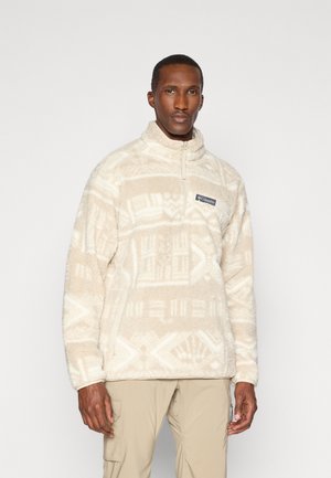 Fleece-pullover i krem med geometriske mønstre. Har en halv glidelås krage og frontlogo-patch. Myk tekstur, avslappet passform.