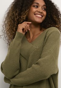 Olivgrüner, gestrickter Pullover mit V-Ausschnitt, der eine Mischung aus gerippten und strukturierten Mustern zeigt, sowie überschnittenen Schultern für eine lässige Passform.