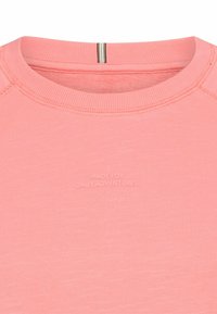 Helles rosa Hemd mit langen Ärmeln und Rundhalsausschnitt, das aus einem strukturierten Stoff besteht und auf der Vorderseite den eingeprägten Text "MADE FOR DAILY ADVENTURES" trägt.