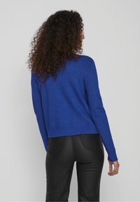 Blue knitted sweater with a round neckline, ribbed hem, and long sleeves, worn over black fitted pants. The texture is soft and smooth.