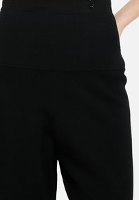 Černé pletené kalhoty s žebrovaným vysokým pasem a postranními kapsami, s hladkým povrchem a minimalistickým designem.