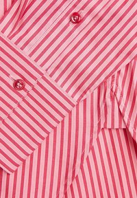 Red and white striped shirt with a pointed collar, featuring button fastenings and a smooth fabric texture. Vertical stripes and tailored details.