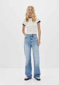 Ljusblå vida jeans med hög midja, kombinerade med en figurnära crèmefärgad t-shirt med svarta detaljer på ärmarna. Svarta skor med accenter.