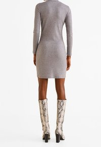 Robe grise à côtes avec des manches longues, longueur genou, associée à des bottes hautes en python avec un talon bloc.