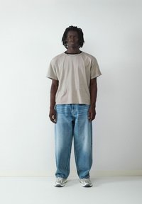 Camiseta de gran tamaño color gris claro con mangas cortas, que presenta un escote redondeado y un sutil detalle de costura, combinada con unos vaqueros de denim azul holgados.