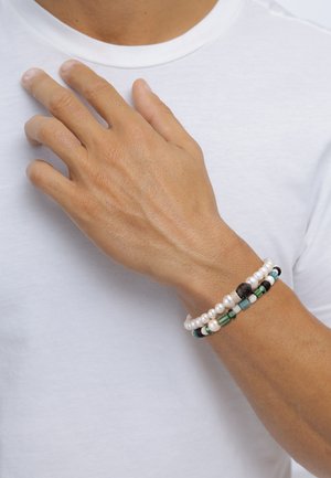 Geflochtener Armband mit weißen Perlen, grünen und schwarzen Perlen sowie filigranen Mustern. Kombiniert mit mehreren Texturen und Farben.