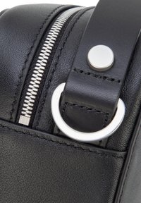 Zwarte leren tas met een zilveren rits, metalen beslag en een ronde accent. Gladde textuur met gedetailleerd stikwerk.