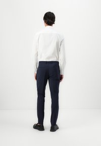 Cămașă albă cu mâneci lungi și pantaloni bleumarin. Cămașa are un design curat, cu un ușor luciu; pantalonii sunt croiți, având buzunare la spate și o textură netedă.