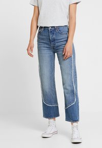 Lyseblå denimjeans med lige ben, frynset kant og kontrastsyningsdetalje, kombineret med hvide high-top sneakers.