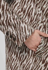 Bruin-wit gestreept mantelstof met een geborstelde textuur, voorzien van een manchet met knopen en een zijzak.