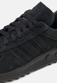 Donkergrijze suède sneakers met een gestructureerd oppervlak, zwarte veters en een gewatteerde kraag. Bevat subtiele branding en een rubberen zool met ronde grippen.