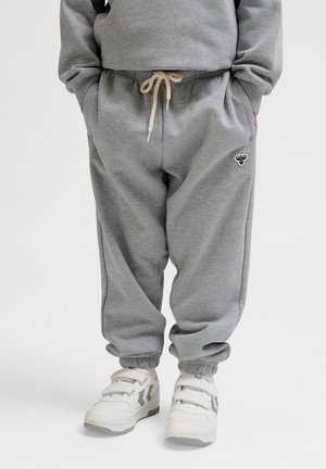 Graue Baumwoll-Sweatpants mit elastischem Bund und beigem Kordelzug, ausgestattet mit Seitentaschen und einem kleinen marineblauen Logodetail. Kombiniert mit weißen Sneakers.