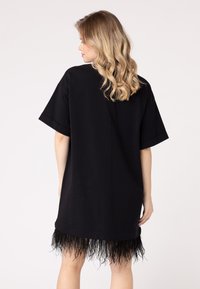 Fekete, oversize t-shirt ruha egyenes szabással és rövid ujjakkal, fekete textúrájú frufru szegéllyel az alján.