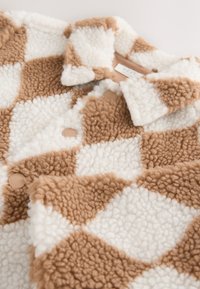 Cappotto in peluche a quadretti marroni e bianchi con una texture morbida e soffice, caratterizzato da un colletto e bottoni rotondi di colore marrone chiaro liscio.