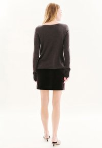 Houten sweater met lange mouwen, ronde halslijn en ribgebreide manchetten, gecombineerd met een zwarte fluwelen rok, wat een slanke silhouet creëert.