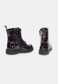 Botas de charol negro con patrones de estrellas multicolores, con cordones en la parte delantera y cremalleras laterales, suelas de goma texturizadas.