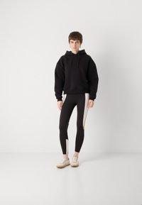 Felpa nera oversize, leggings neri aderenti con pannelli laterali beige e scarpe chiare. Tessuto morbido con un design sportivo casual.