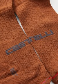 Chaussettes de cyclisme en maille marron avec un motif texturé, portant le logo "Castelli" en gris. Détail rouge au niveau du bord. Côtes pour le confort.