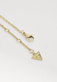 Collana in oro con ciondolo triangolare con la scritta "GUESS" e un punto interrogativo, chiusa con moschettone.