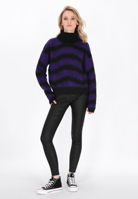 Maglione a righe viola e nero con colletto alto, abbinato a pantaloni neri aderenti e sneakers alte nere con dettagli bianchi.