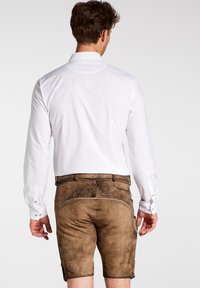 Camisa blanca de manga larga combinada con pantalones cortos de cuero marrón con bordados decorativos y detalles de costura, mostrada desde la parte de atrás.