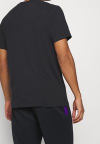Camiseta de algodón negra con mangas cortas, cuello redondo y una textura suave. Presenta un diseño minimalista sin logotipos ni acentos visibles.