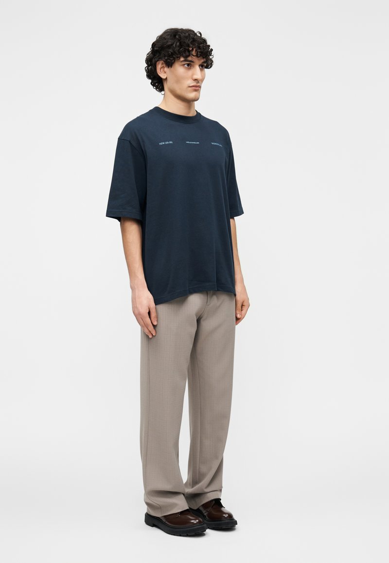 Marinblå oversized t-shirt med korta ärmar, med diskret text på bröstet, kombinerad med ljusbeige plisserade byxor och svarta skor.