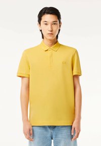 Gul kortärmad polo med krage, med en subtil logotyp på bröstet. Tillverkad av lätt tyg med en mjuk yta.