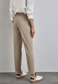 Pantaloni beige realizzati in tessuto leggero, con una vestibilità comoda, due tasche posteriori e abbinati a scarpe da ginnastica casual bianche e nere.