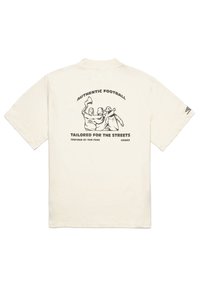 Cream-colored short-sleeve t-shirt featuring a black graphic illustration of three figures, with text "AUTHENTIC FOOTBALL TAILORED FOR THE STREETS."