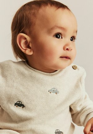 Knit baby sweater in cream with round neck. Features embroidered cars in blue and black. Wooden button accent on shoulder adds detail.