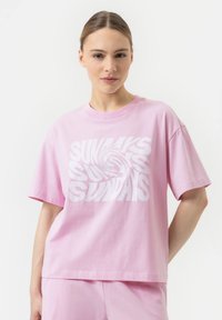T-shirt rose à manches courtes en coton, avec un grand texte graphique en blanc en spirale "SUNDAYS" centré sur le devant.