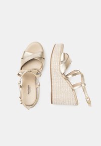 Sandali wedge metallici dorati con cinturini incrociati, una piattaforma con texture intrecciata e una cinghia alla caviglia regolabile. Rivestimento interno liscio.