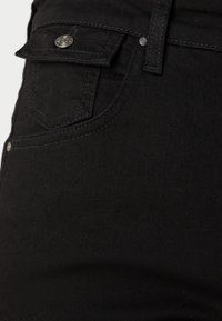 Jean noir avec une texture lisse, comportant une poche avant avec un rabat, des accents de bouton argenté et des coutures contrastées sur les coutures.