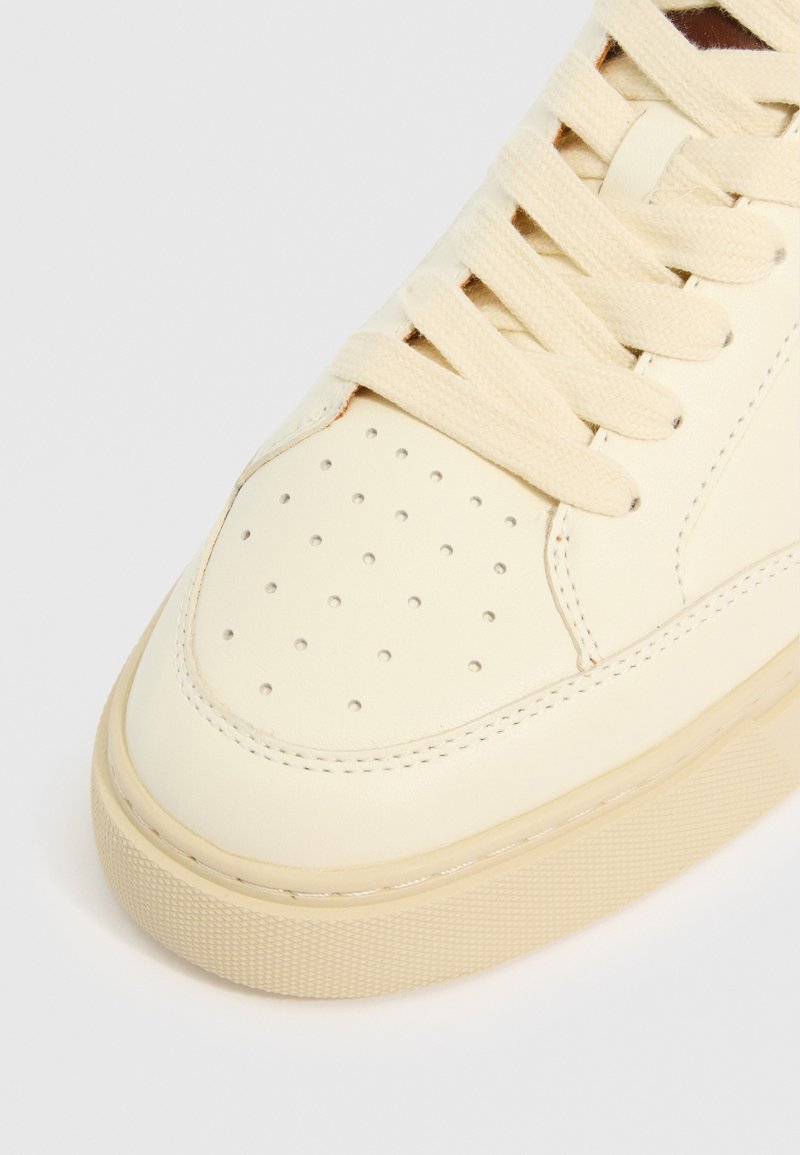 Cremfarbene Leder-Sneaker mit perforiertem Zehenbereich, flachen Schnürsenkeln und einer strukturierten Gummisohle mit dezenten Näheinheiten.