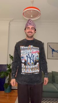 Juodas džemperis su „World Series“ senu grafiniu dizainu, kuriame pavaizduotas Niujorko „Yankees“ logotipas. Violetinė kepurė, laisvas siluetas, matoma tekstūra.