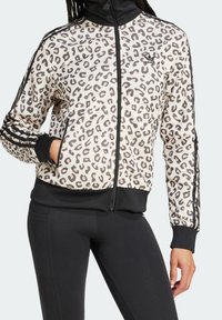 Leopardmönstrad zip-up jacka i kräm och svart, med sidofickor, ribbade ärmslut och nederkant, samt tre svarta ränder på ärmarna.