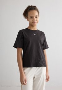 Čierne bavlnené tričko s krátkymi rukávmi, s mal�ým bielym logom Puma na hrudi, skombinované so svetlými nohavicami.