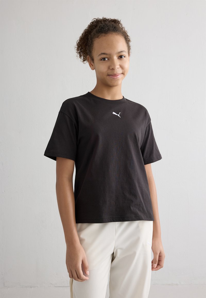 Čierne bavlnené tričko s krátkymi rukávmi, s malým bielym logom Puma na hrudi, skombinované so svetlými nohavicami.
